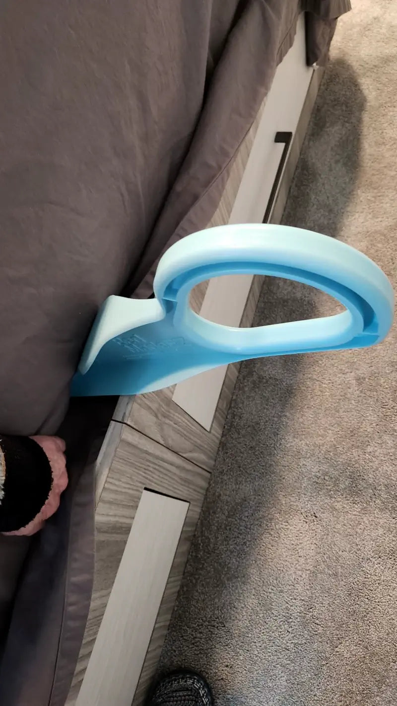 Close-up of a hand placing a light blue mattress lifter under a mattress beside a grey bed frame